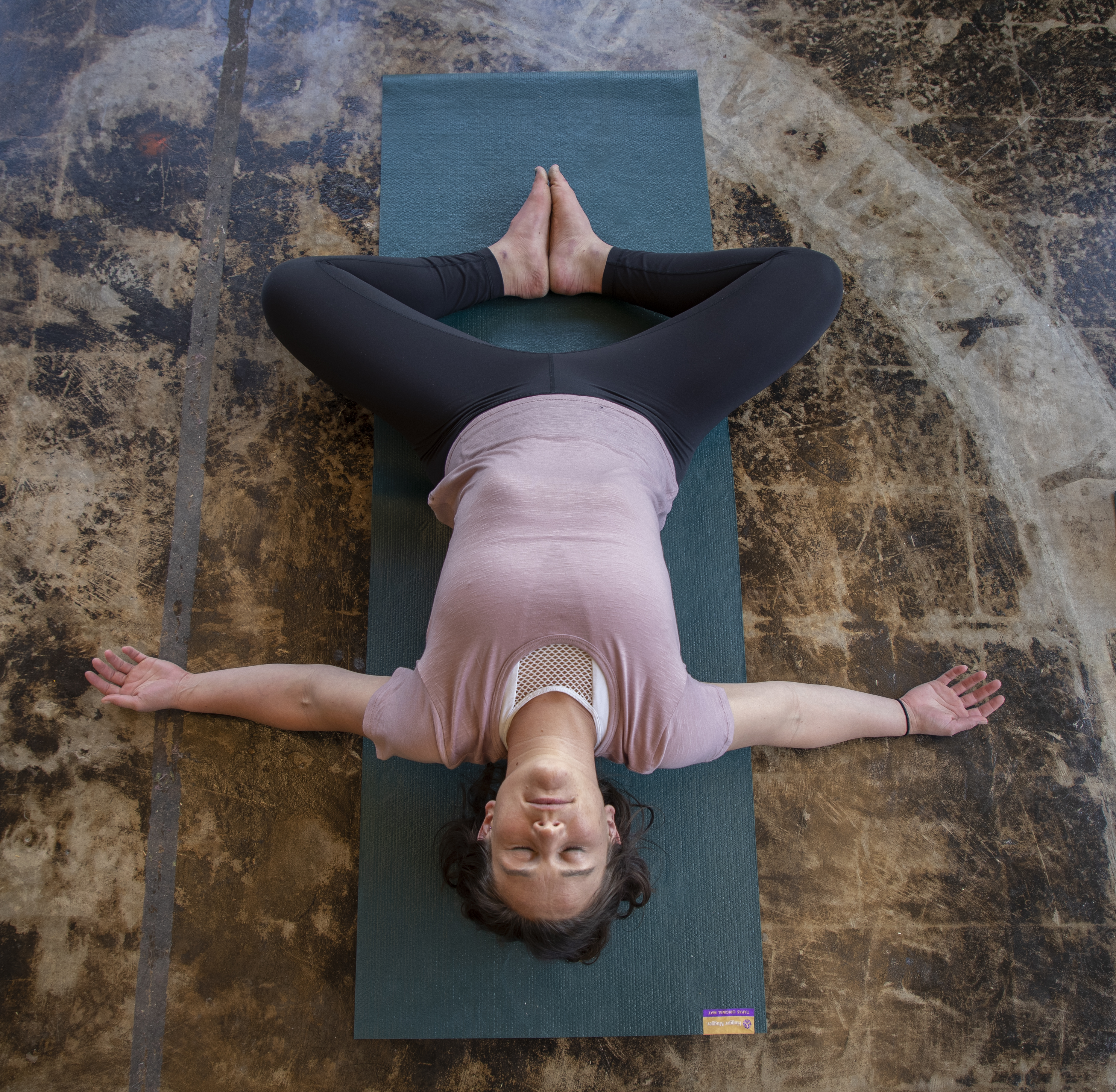 Overhead view of Elly in a restorative yoga pose on a teal mat