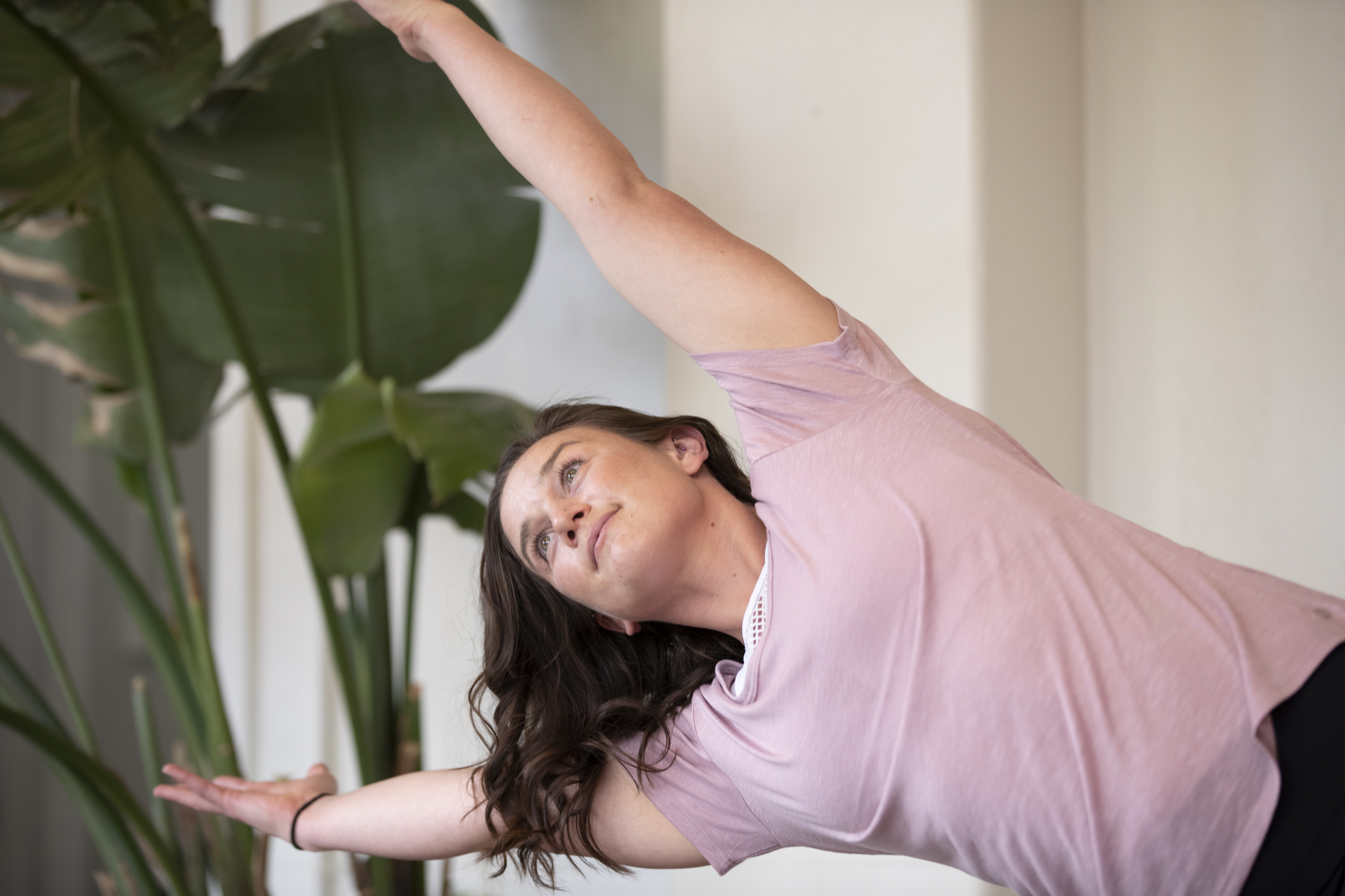 Elly performing a side stretch yoga pose with plants and natural light in the background