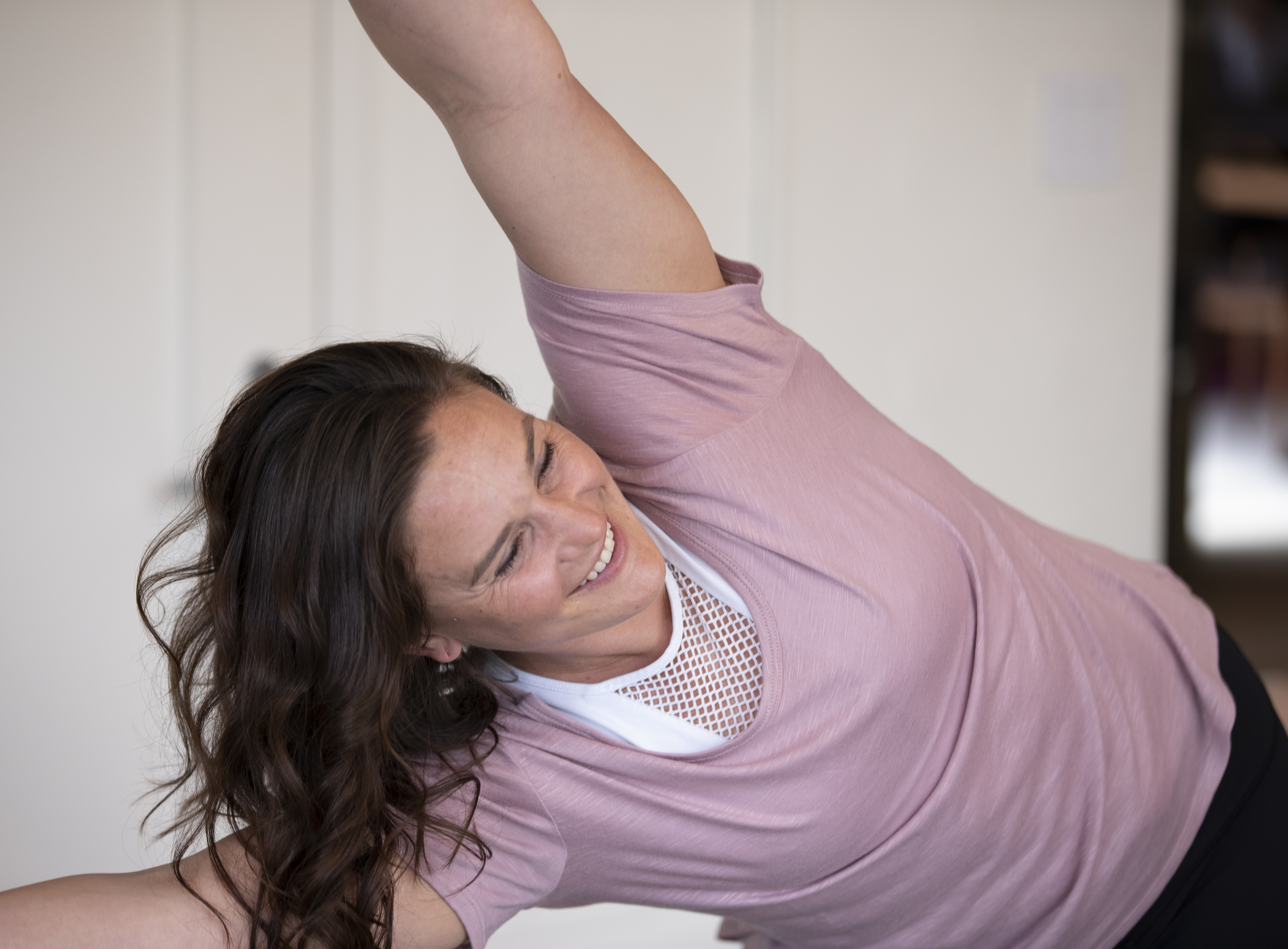 Elly smiling while practicing a side angle yoga pose in her Denver studio with plants in the background