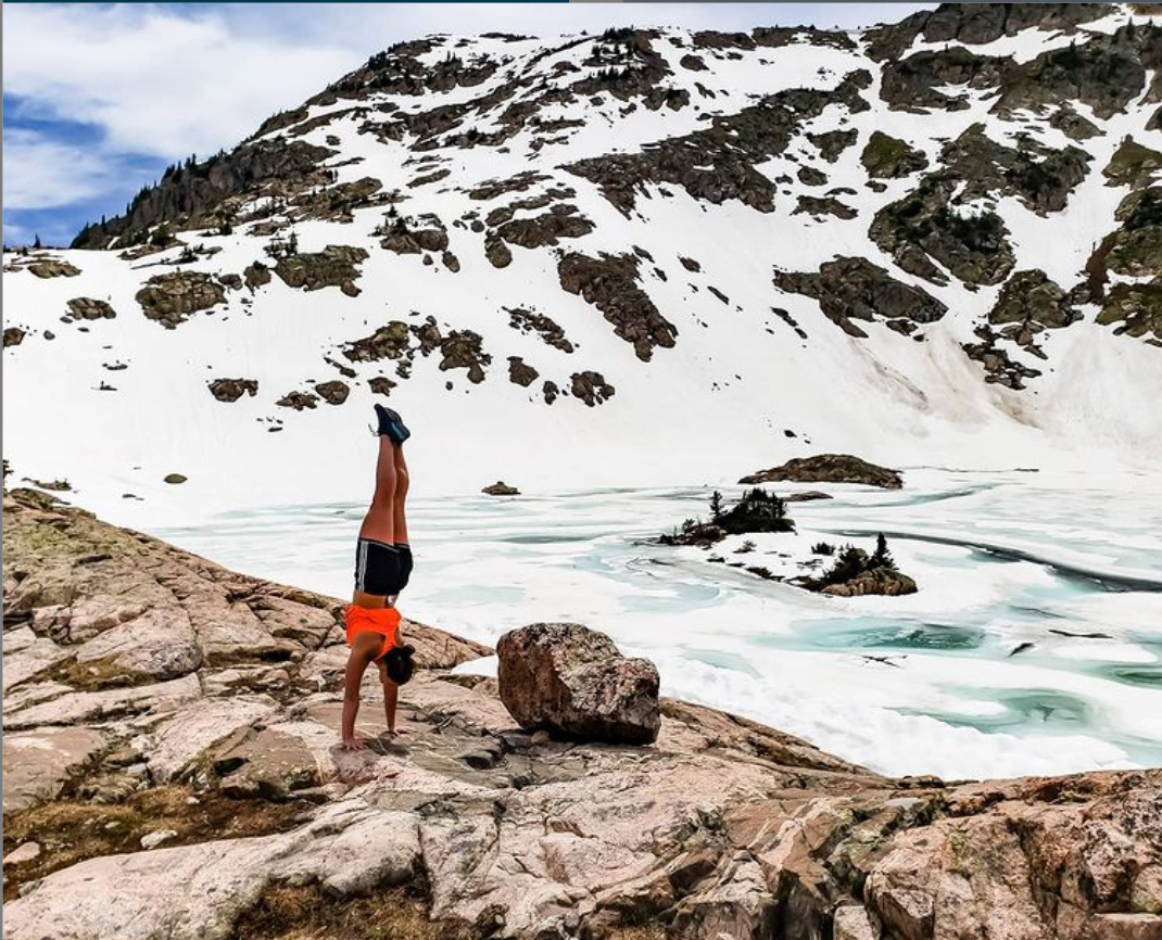 Elly doing a handstand in the Colorado mountains with a frozen alpine lake in the background